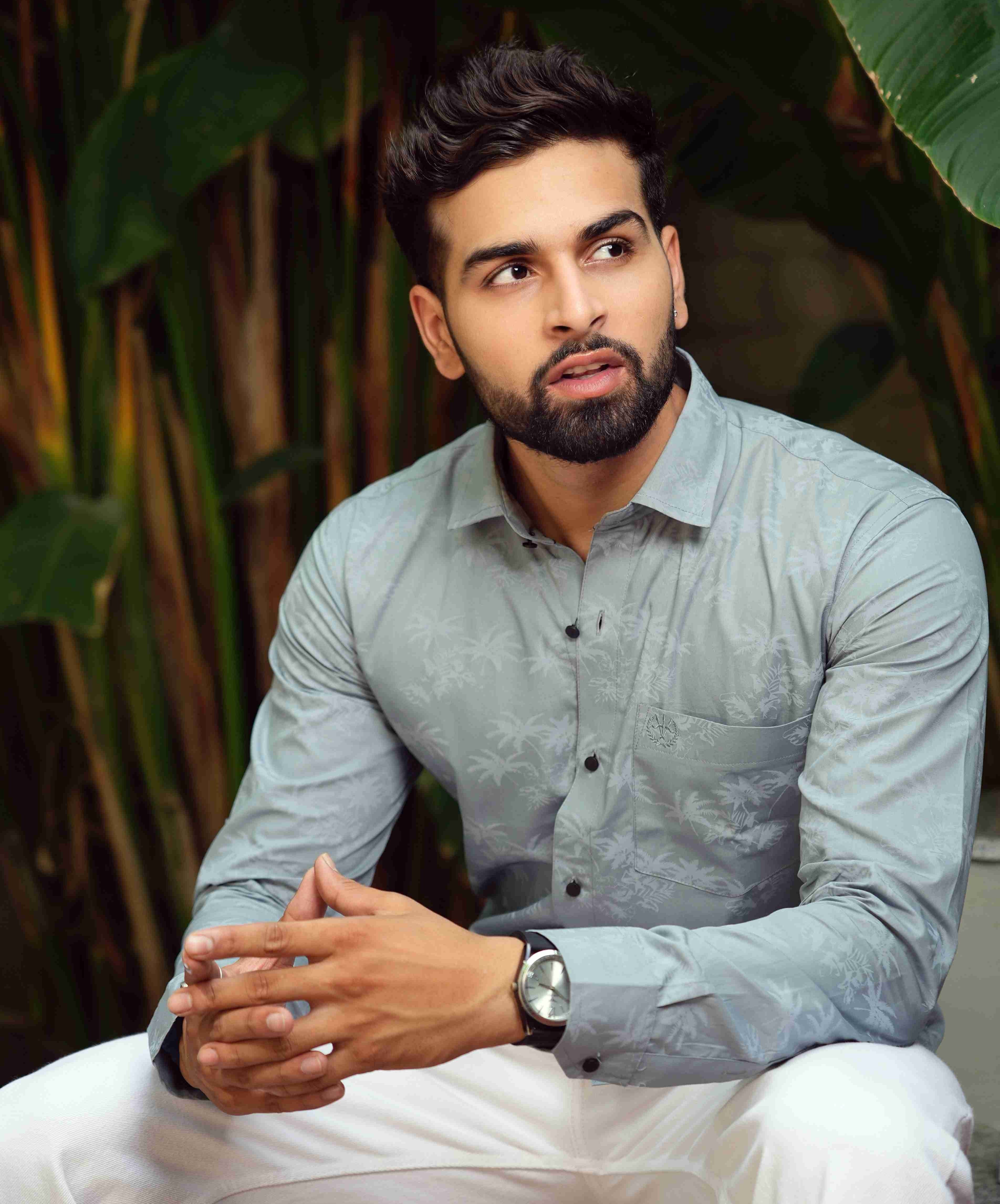 formal_shirt_-_Amerald_arrows Man wearing a light blue shirt and white pants sitting among green plants