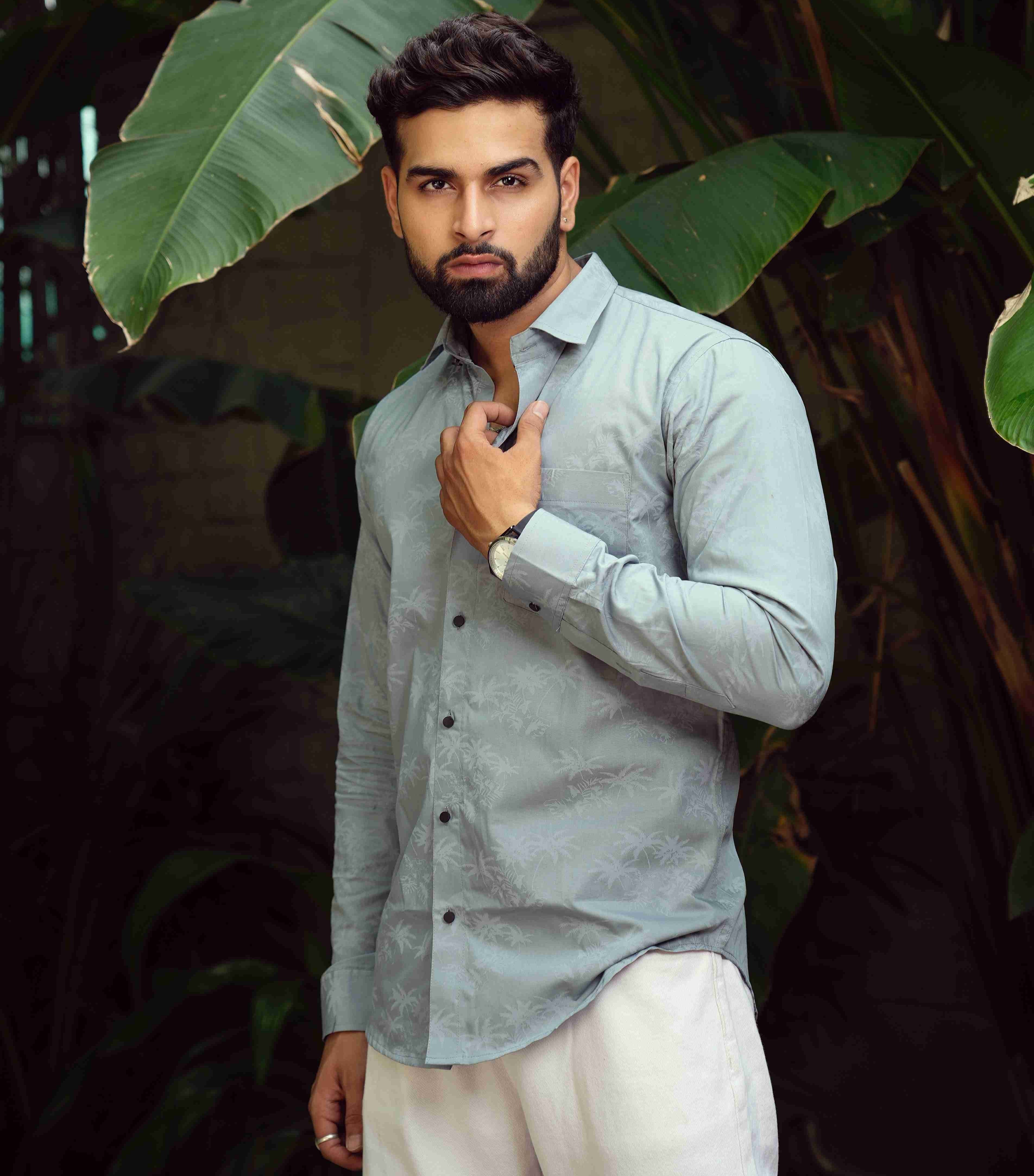 Man in light gray shirt and white pants standing among large green leaves
