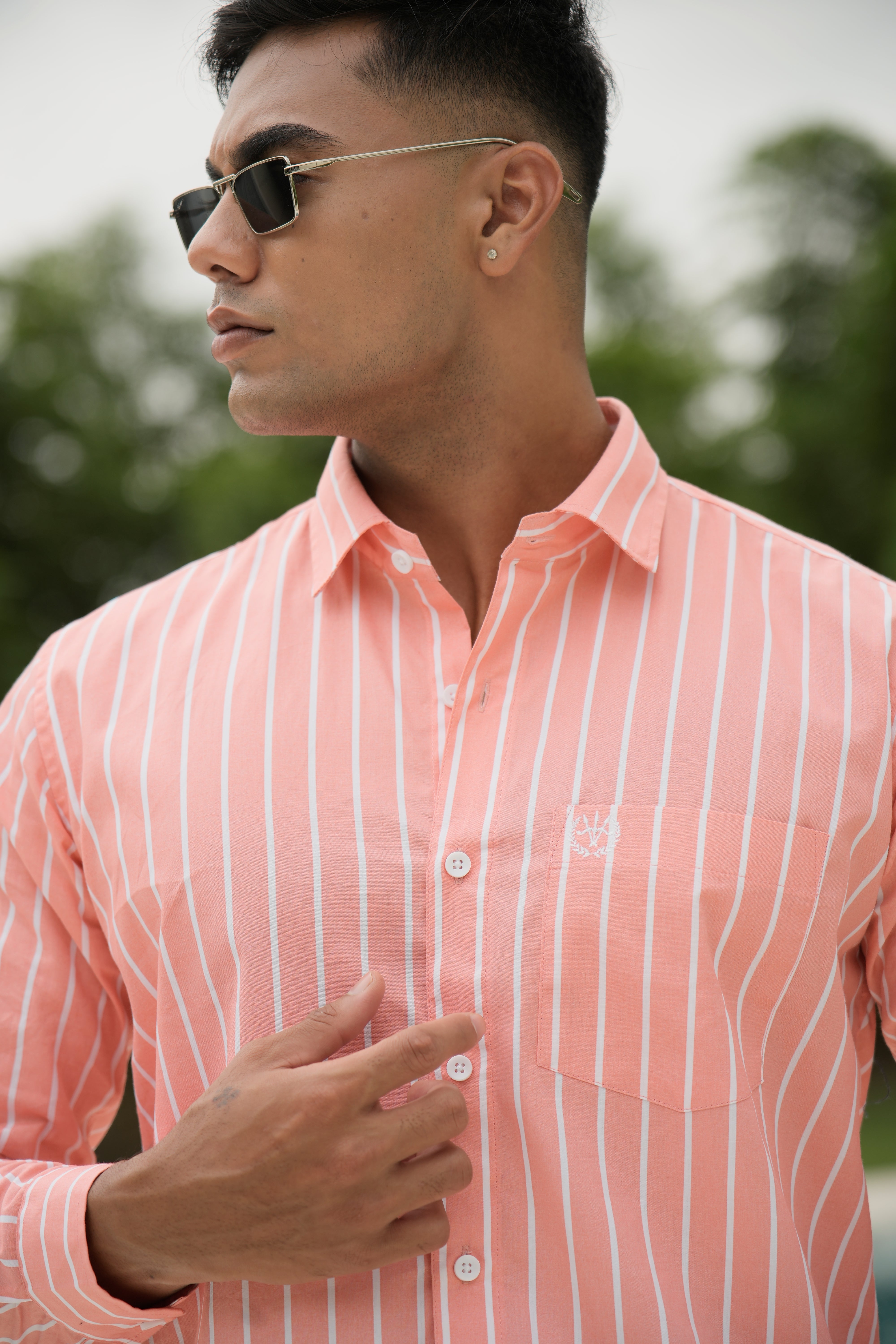 Amerald_arrows Man wearing a pink striped shirt and sunglasses with a blurred green background