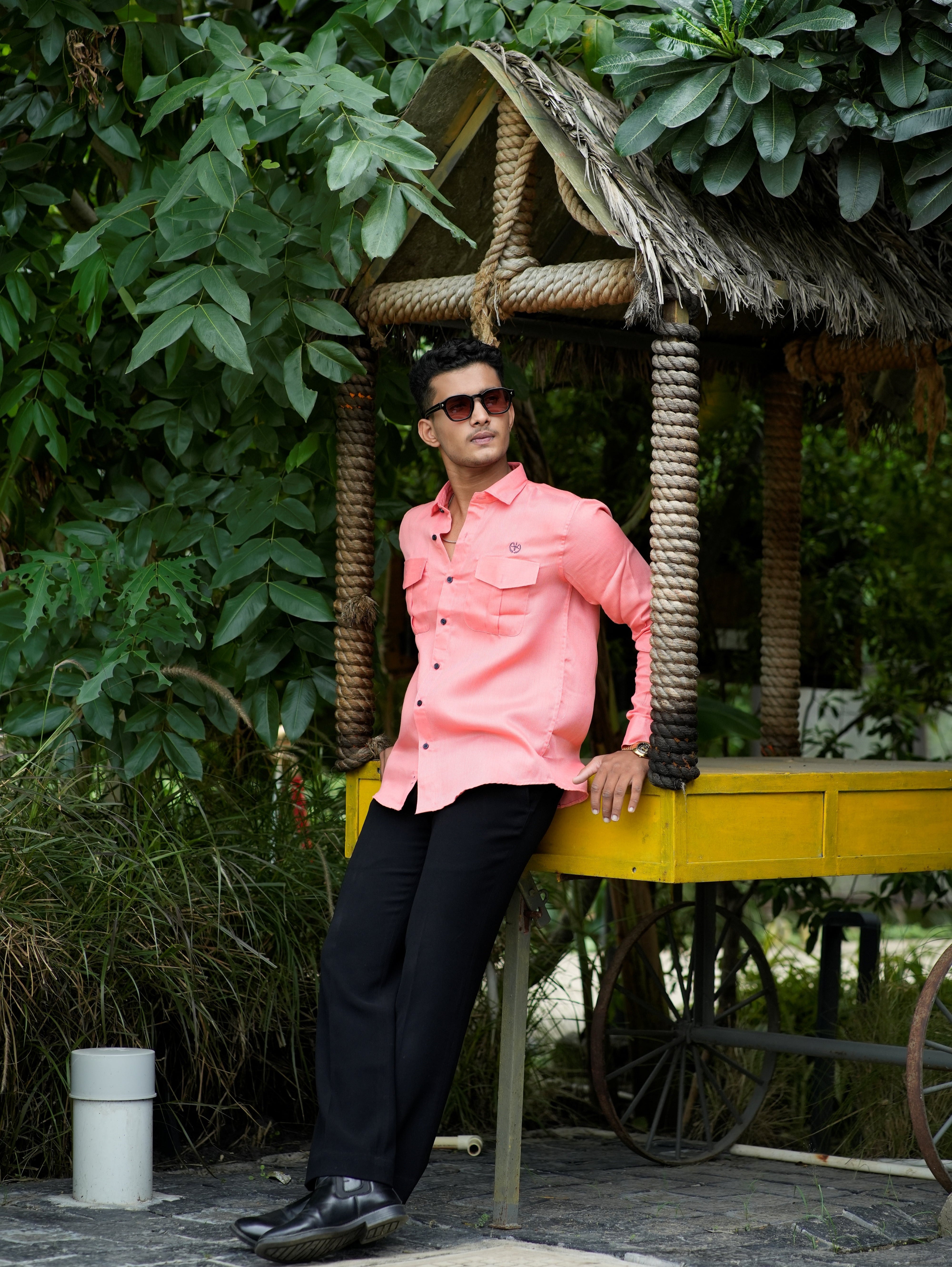 Person in a pink jacket standing next to a wooden structure with greenery around